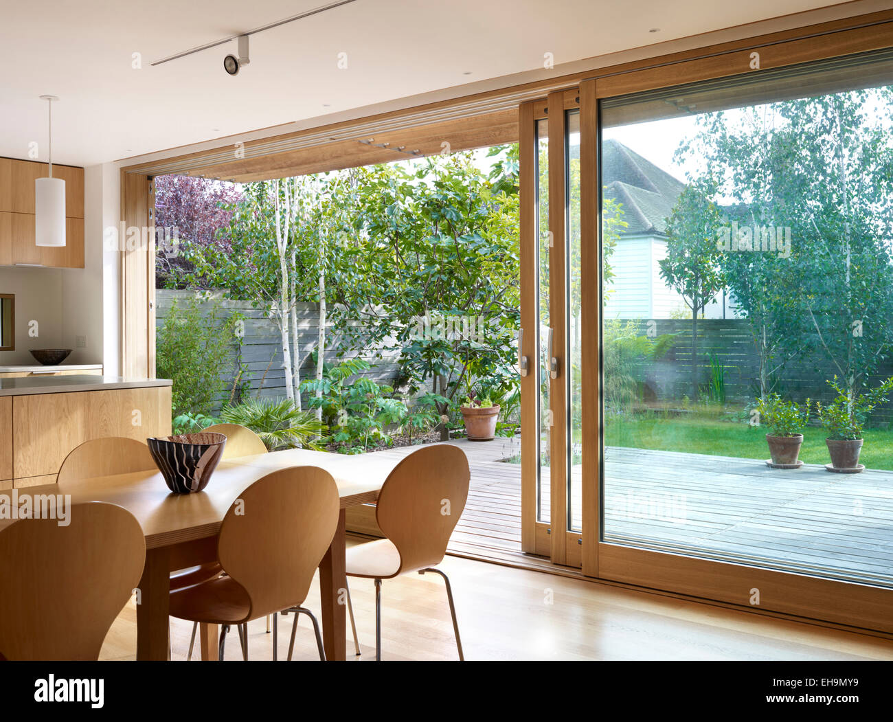 Mesa de comedor y sillas de madera delante de grandes puertas corredizas de vidrio, casa residencial, Lloyd cerca, REINO UNIDO Foto de stock