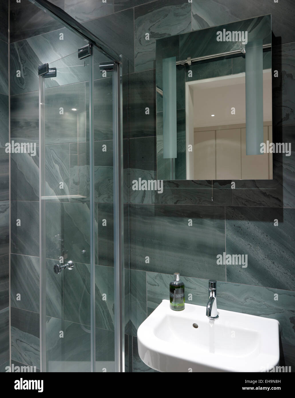 Baldosas estampadas moderno iluminado cuarto de baño con cabina de ducha de cristal puerta y cuenca en Walham Grove, hogar, REINO UNIDO Foto de stock