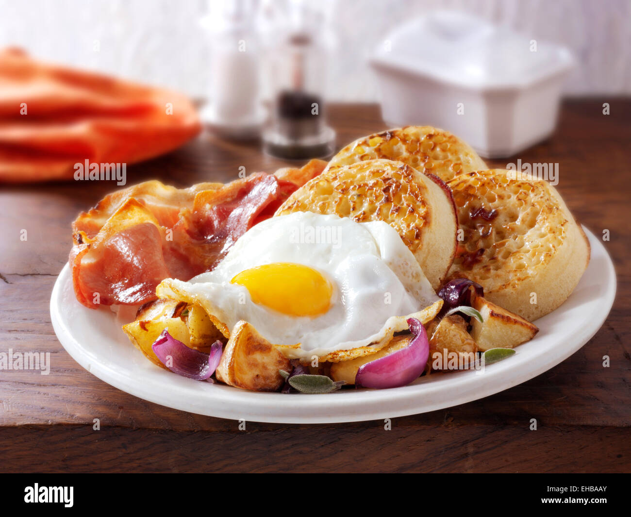 Desayuno inglés completo con crumpets, servido en una placa blanca en un ajuste de la tabla - huevo frito, bacon, patatas salteadas y crumpets Foto de stock