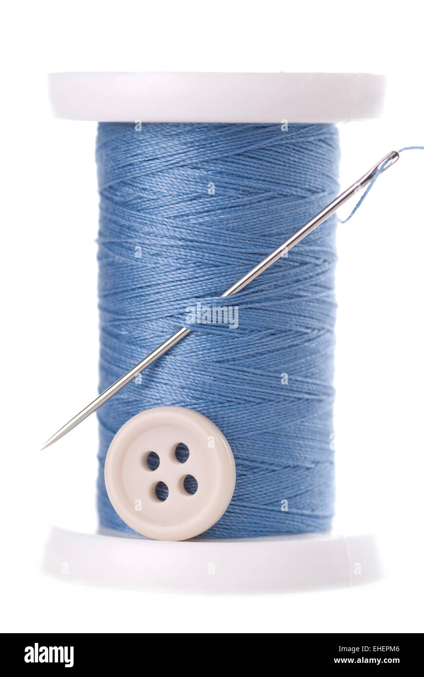 Una bobina de hilo azul con aguja y un botón blanco. Foto de stock