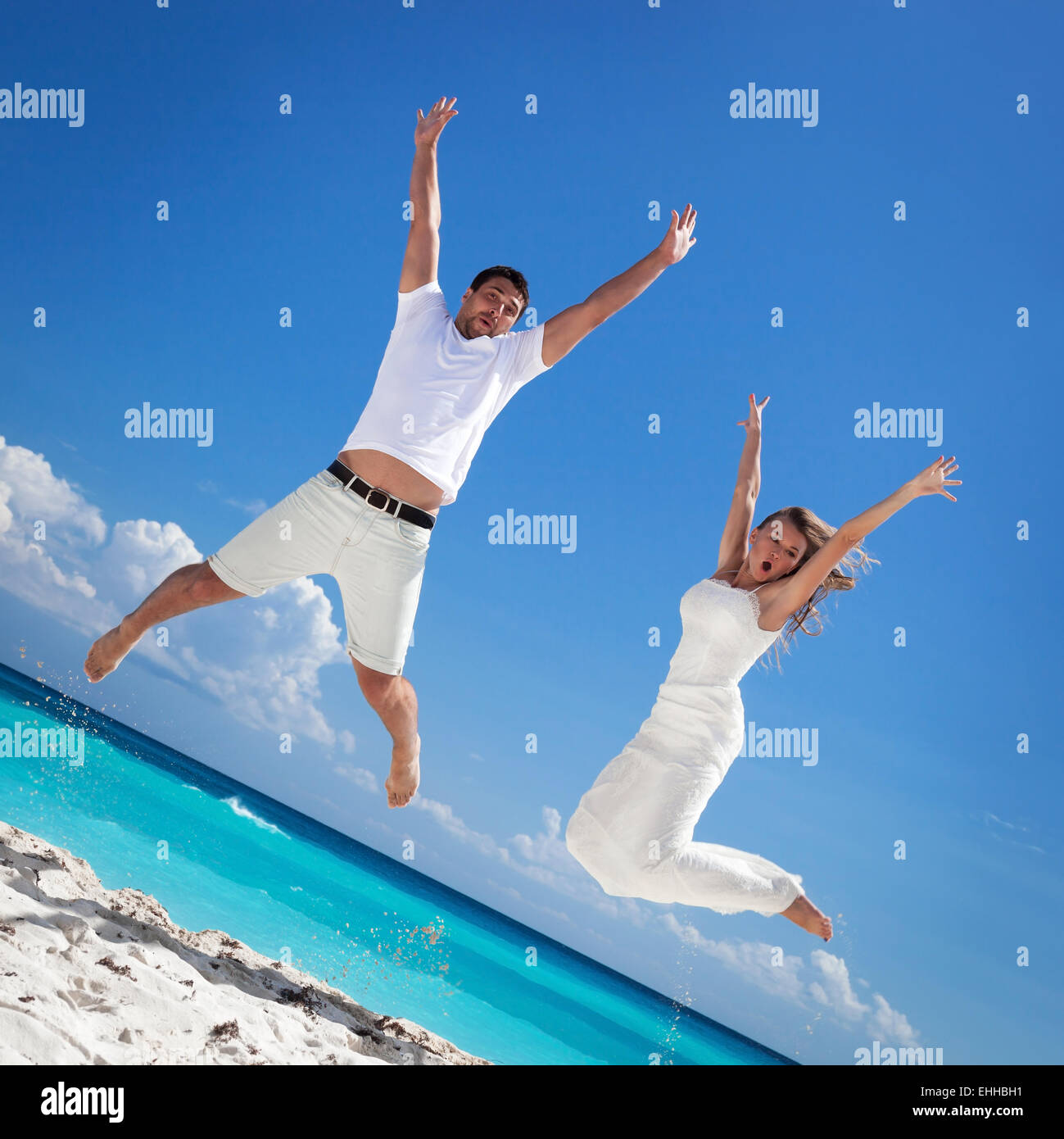 Los recién casados feliz saltando en la playa con fondo de cielo azul Foto de stock