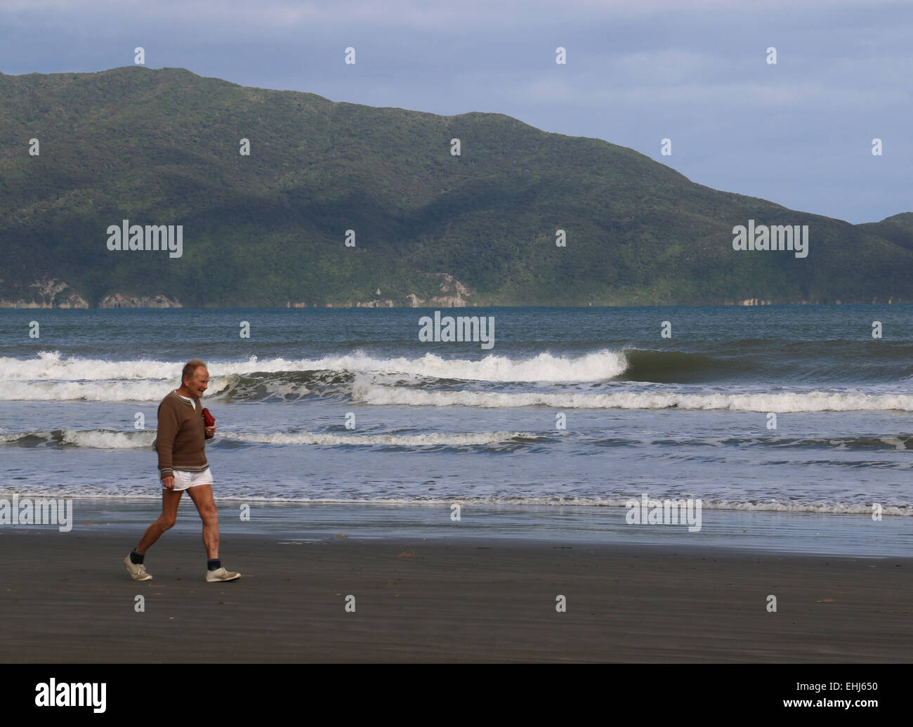 Los ciudadanos senior trotar en Waikanae playa cruzando la Isla Kapiti en fondo, Nueva Zelanda Foto de stock