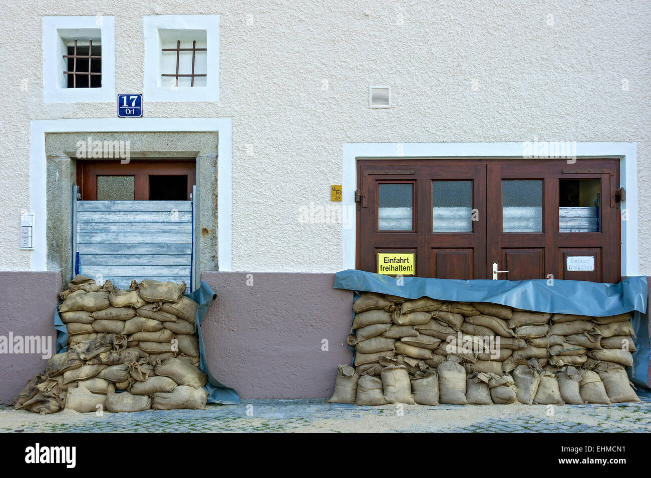 Medidas de control de inundaciones, sacos de arena y un muro protector de listones de acero delante de una puerta delantera y una puerta de garaje Foto de stock