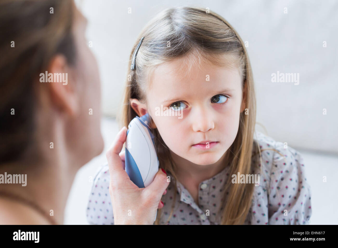 Controlar la temperatura de una niña de 4 años con el termómetro de oído. Foto de stock