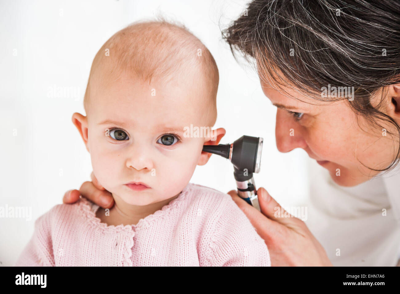 El pediatra examina la oreja de un bebé de siete meses a una chica con un otoscopio. Foto de stock
