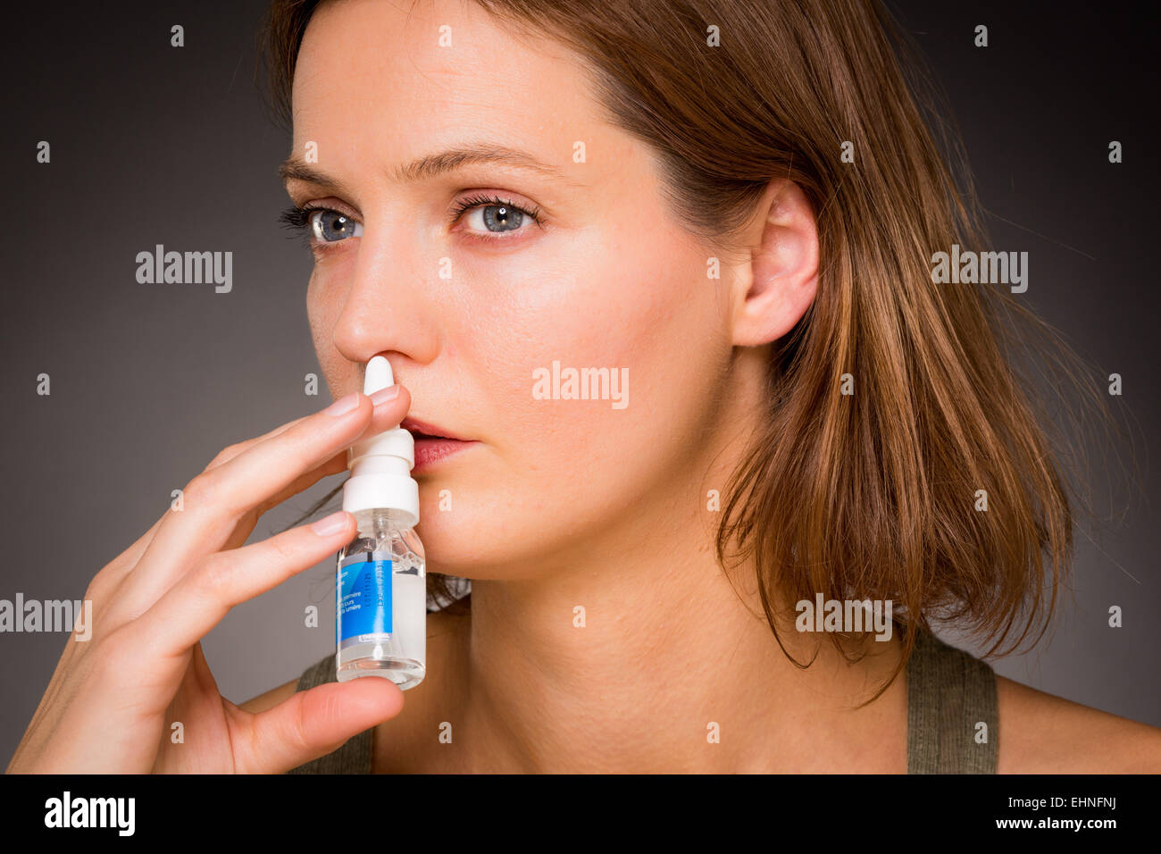 Mujer con aerosol nasal para controlar la rinitis. Foto de stock