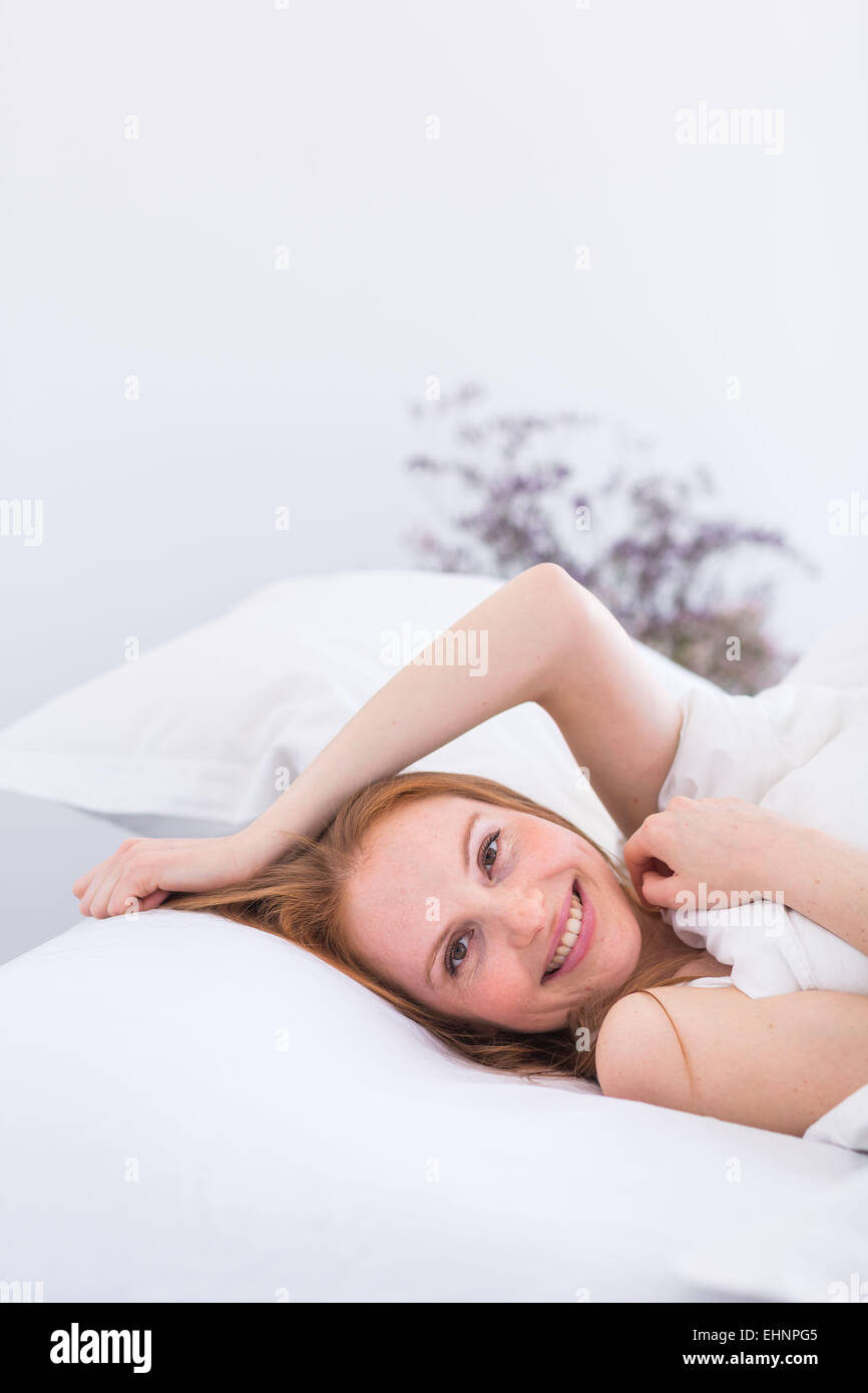 Mujer recostada en la cama, la cabeza en la almohada, sonriendo a la cámara Foto de stock