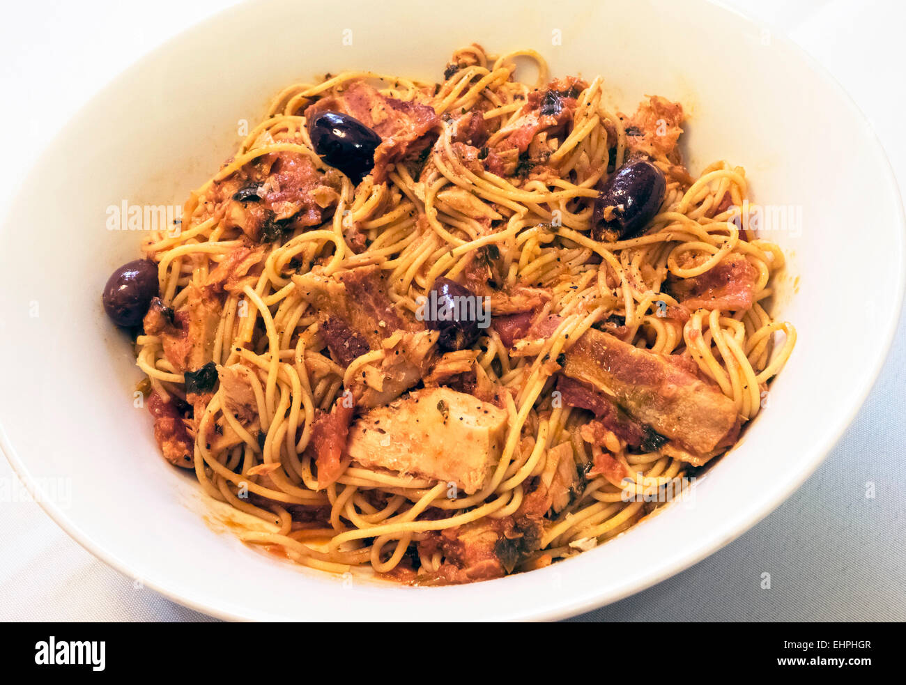 Espaguetis con atún, bacon, aceitunas y salsa de tomate en un recipiente blanco Foto de stock