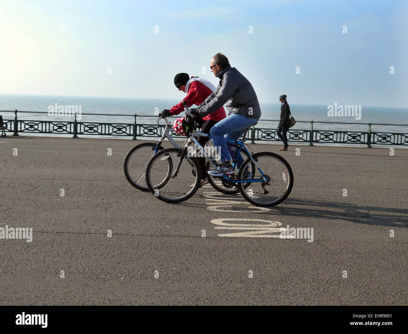 Dos ciclistas, no llevar cascos, ignorar a ningún signo de ciclismo pintado sobre el asfalto mientras el ciclismo en Hove promenade, en la ciudad de Brighton y Hove, East Sussex Foto de stock