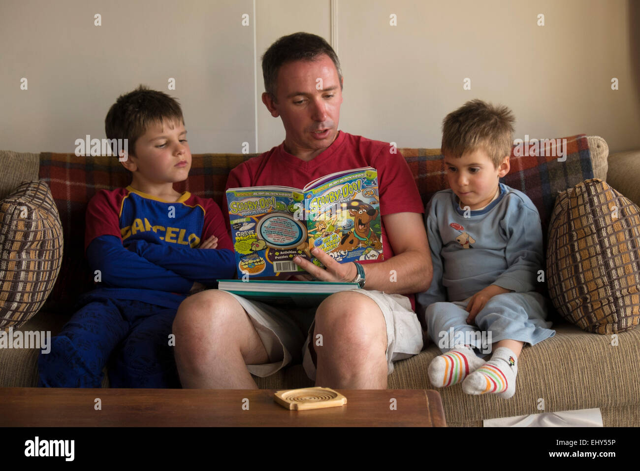 Padre leyendo a sus hijos en el sofá en casa Foto de stock