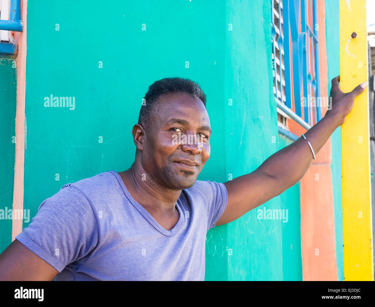 Un hombre afrocubano se inclina con su brazo contra paredes de colores brillantes de la parte exterior de las casas vecinas. Foto de stock