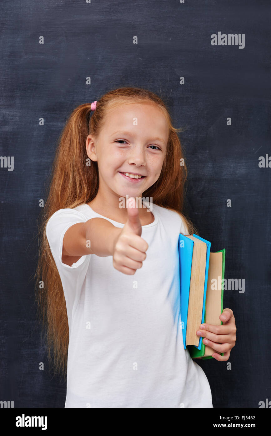 Jengibre sonriente chica con libros y mostrando Thumbs up Foto de stock