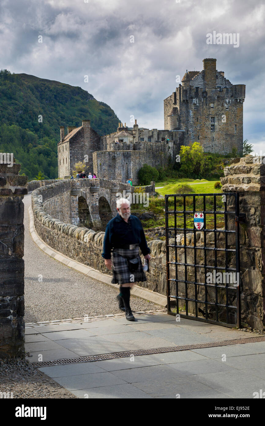 Hombre en una falda cruza el puente desde el castillo de Eilean Donan, Highlands, Scotland, Reino Unido Foto de stock