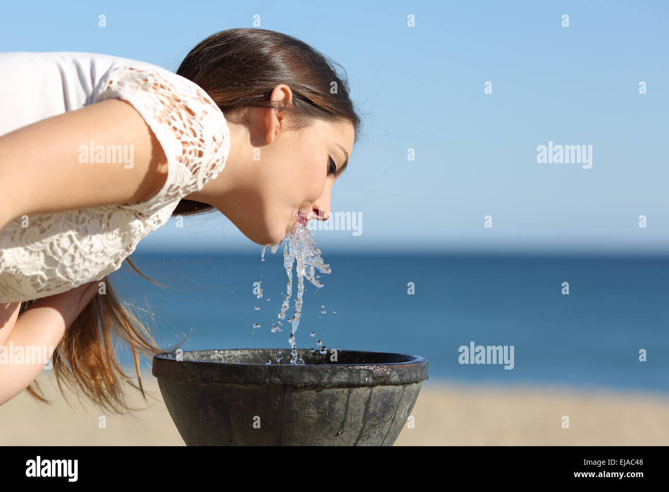 Mujer sedienta de beber agua de una fuente en la playa en un día soleado Foto de stock