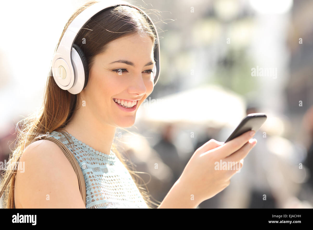 Mujer escuchando música con auriculares inalámbricos desde un teléfono  inteligente en la calle Fotografía de stock - Alamy