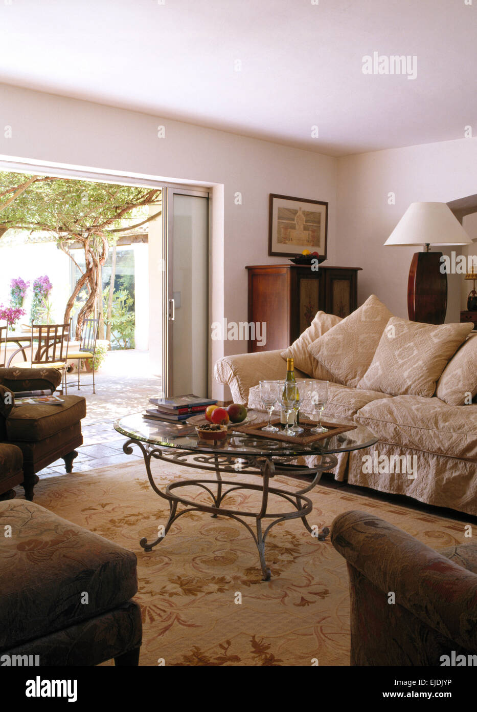 Vidrio Metálico rematado mesa de café y un sofá grande con tapa suelta beige en francés país salón con puertas abiertas al jardín. Foto de stock
