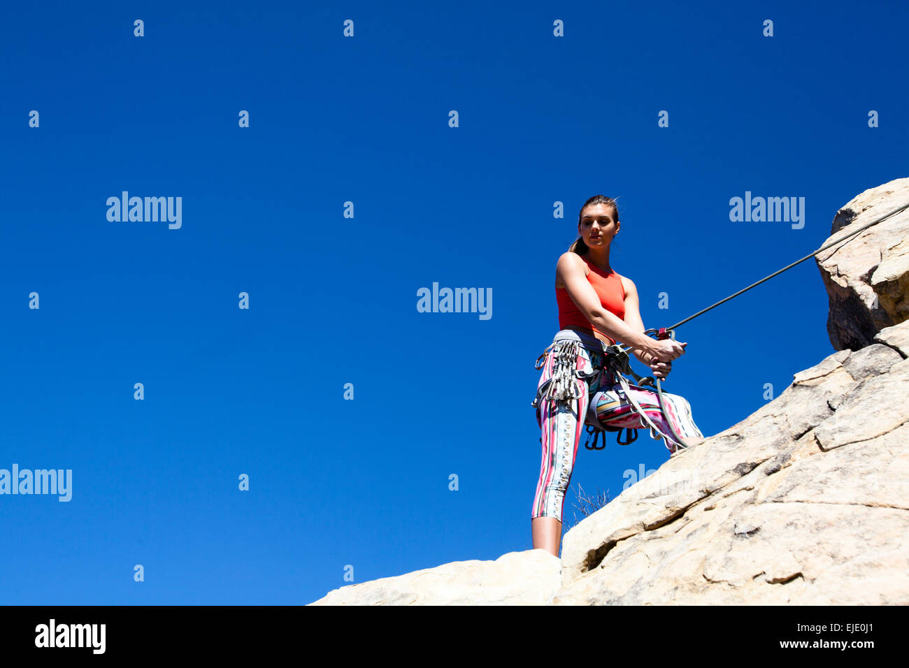 Una mujer vistiendo un tank top rojo y pantalón rayado belays Gibraltar inferior mientras que la escalada en roca en Santa Bárbara, California. Foto de stock