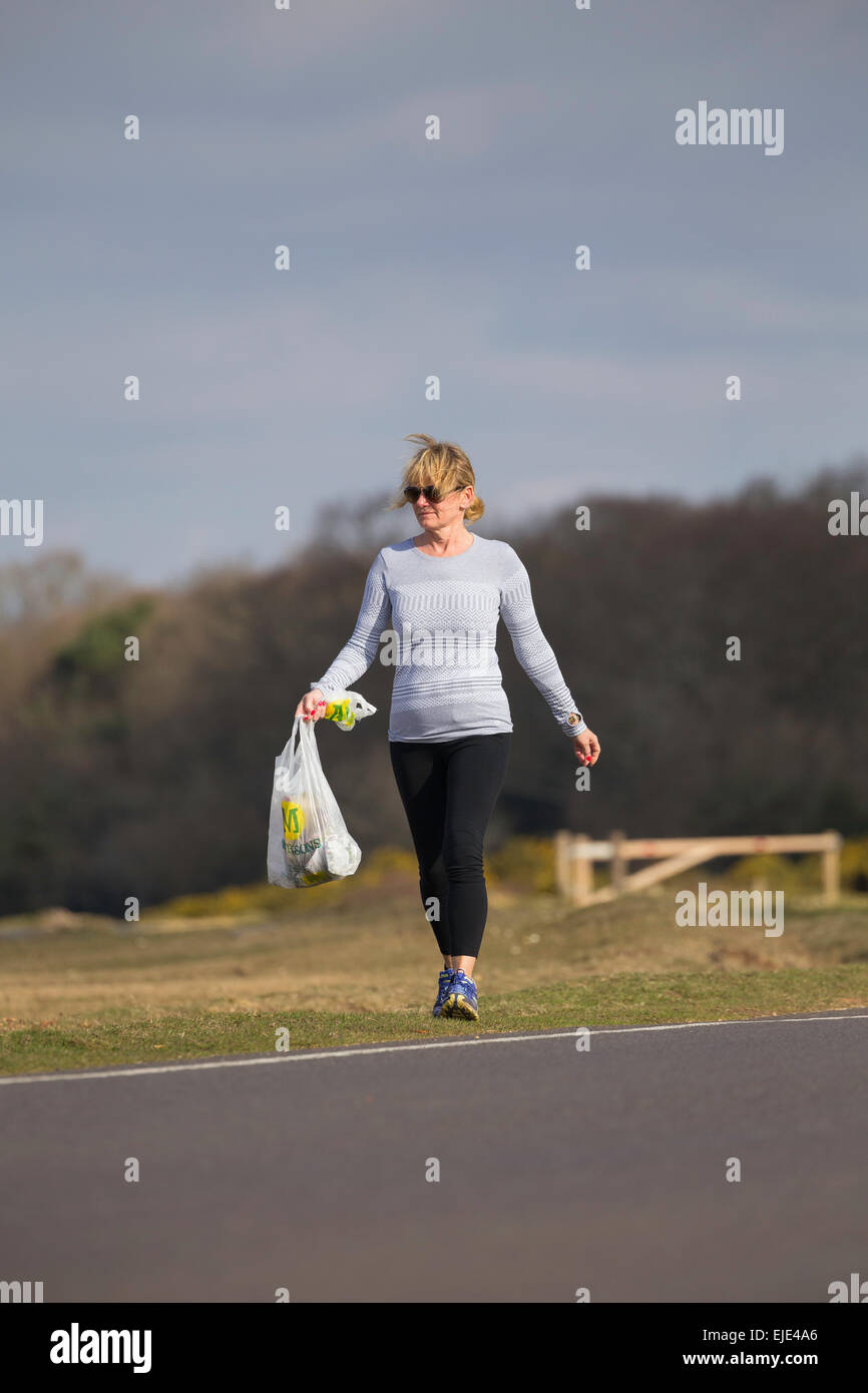 Una mujer de edad es jogging en el Parque Nacional de New Forest llevando un par de Morrison's bolsas para recoger la basura. Foto de stock