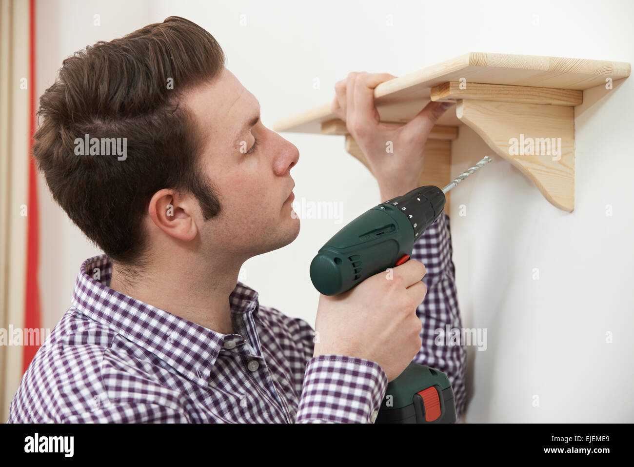 Hombre haciendo un estante de madera en su hogar con taladro sin cable eléctrico Foto de stock