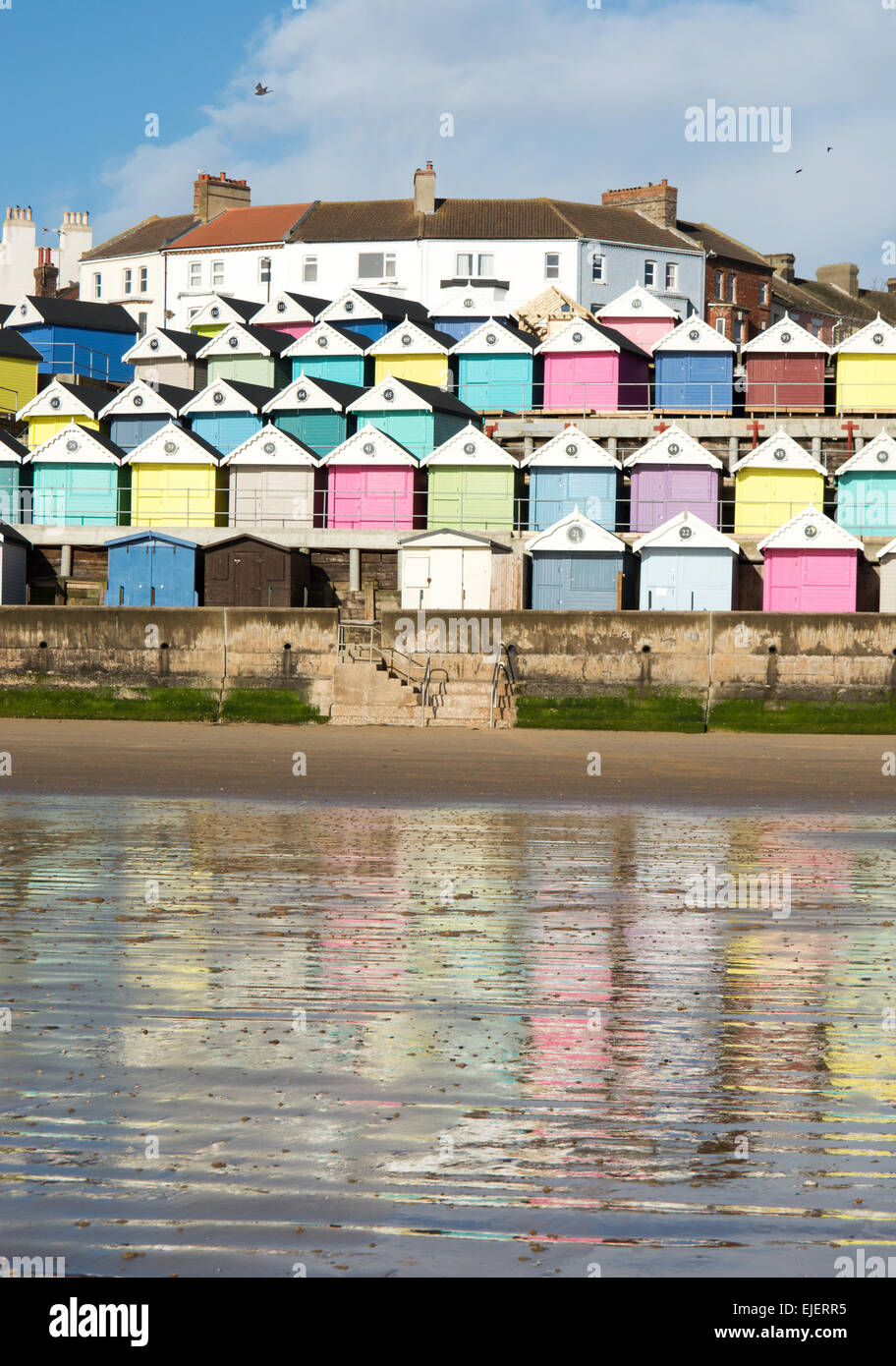 Una colorida selección de cabañas de playa que se han creado cerca de Walton en el Naze se reflejan en la playa de arena húmeda. Foto de stock