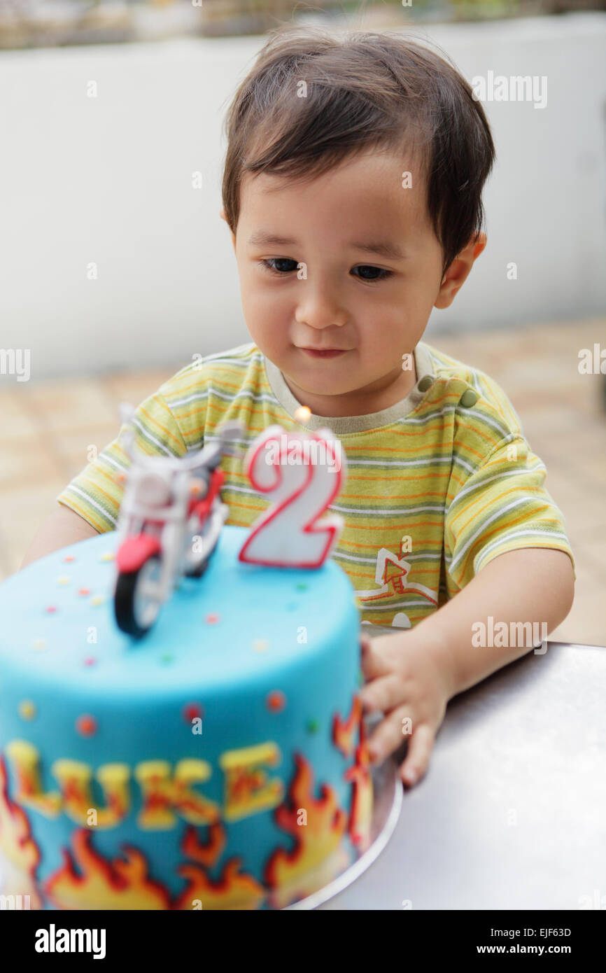 Niño boy girando dos años, soplando las velas de su pastel de cumpleaños Foto de stock