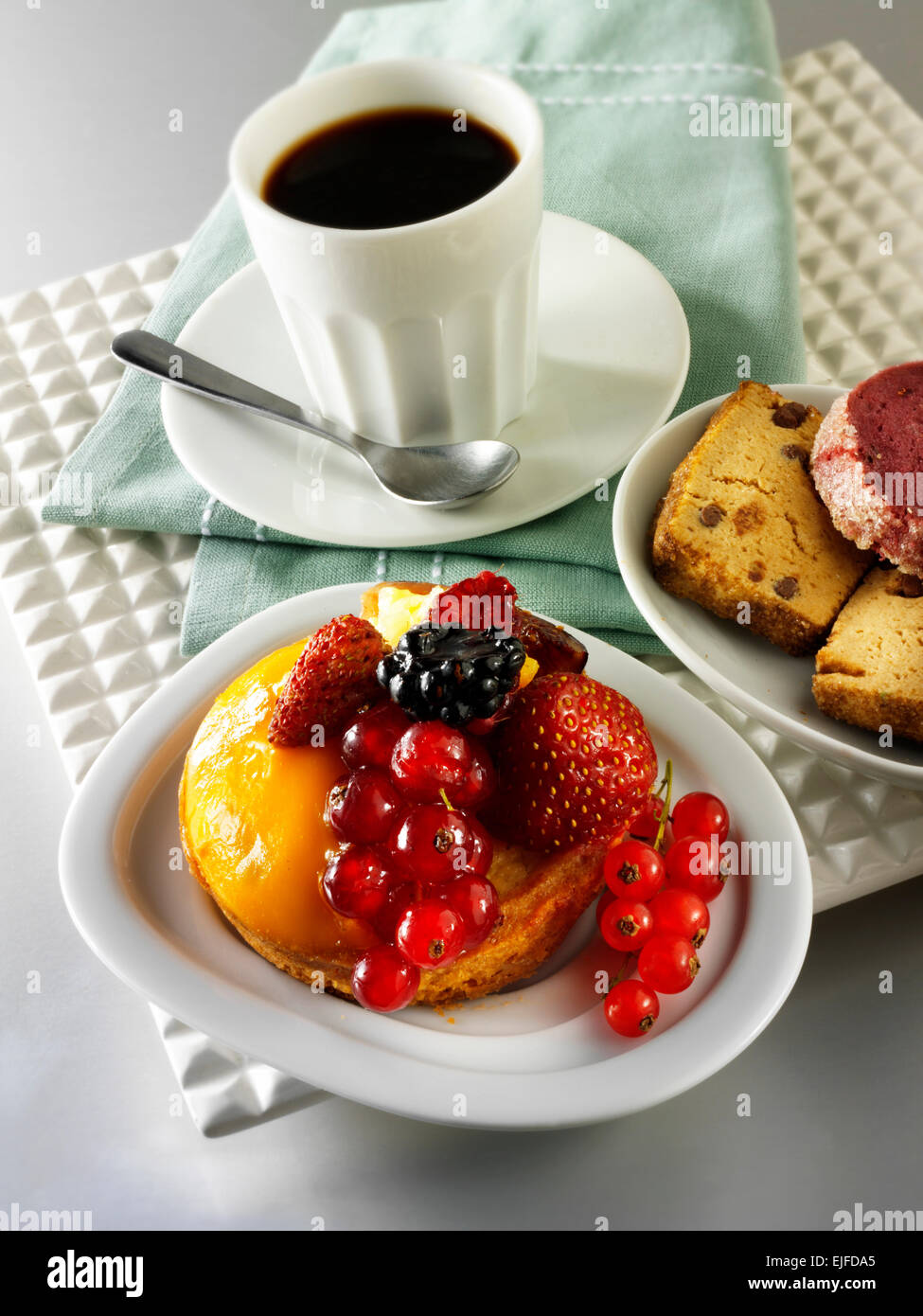 Pastel de frutas con grosellas, fresas silvestres, blackberry y crema de pastelería en un caso de esponja de luz en un café con la taza de café Foto de stock
