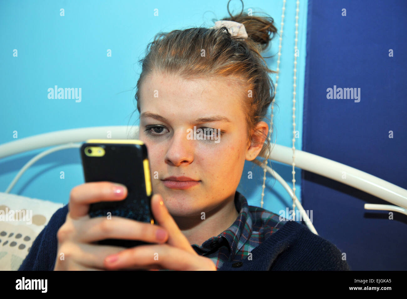 Adolescente comprueba facebook y twitter en su teléfono móvil en su dormitorio Foto de stock