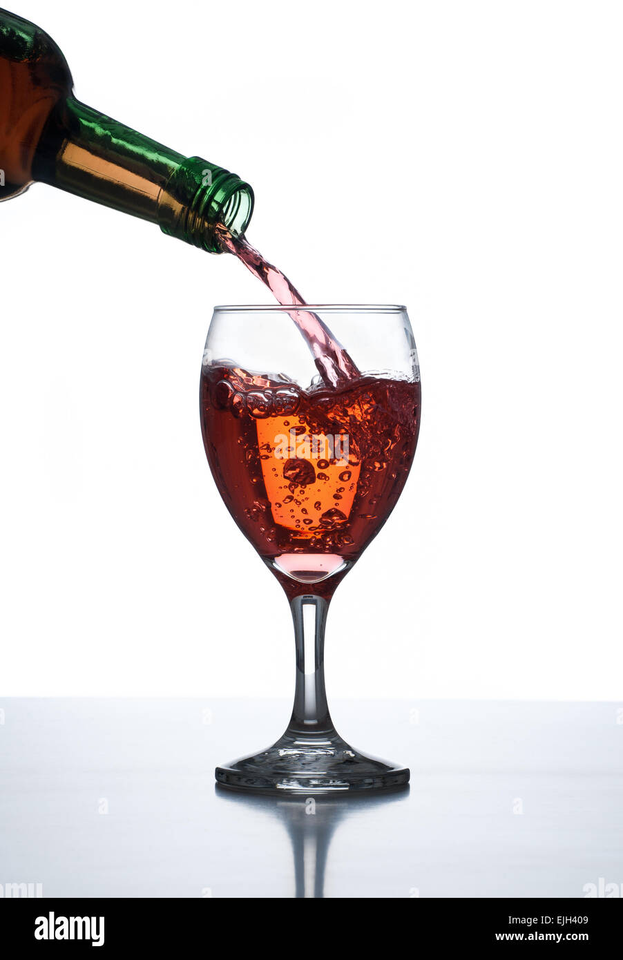 Verter el licor en vaso de vino de mesa reflectante con fondo blanco. Foto de stock