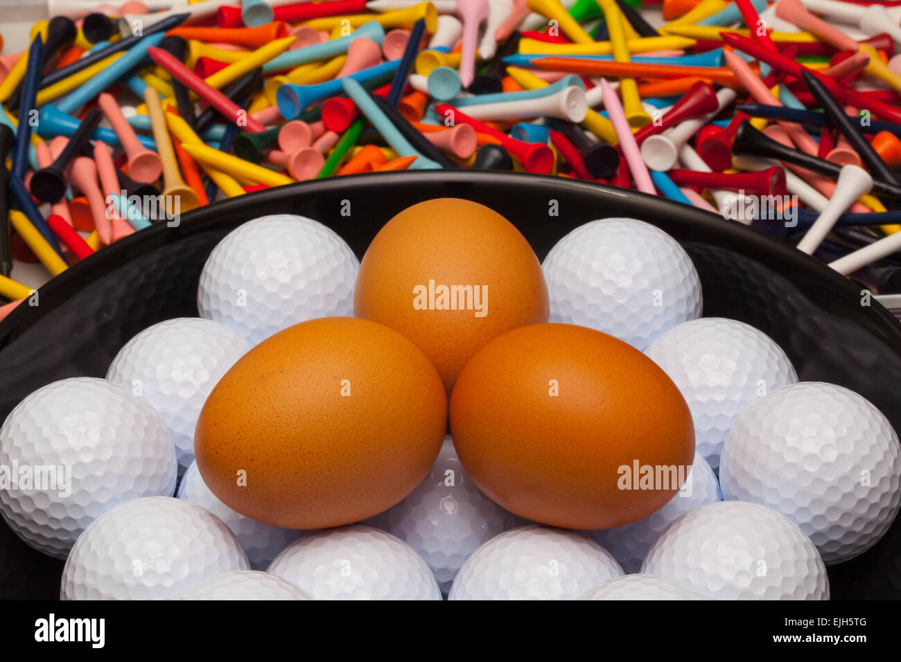 Las bolas de golf y los huevos en un recipiente negro Foto de stock