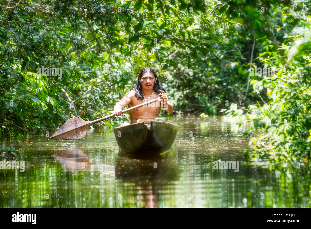 Hombre adulto indígena en típicas canoas de madera de un solo árbol picada Navegando aguas turbias de Selva Amazónica Ecuatoriana Foto de stock