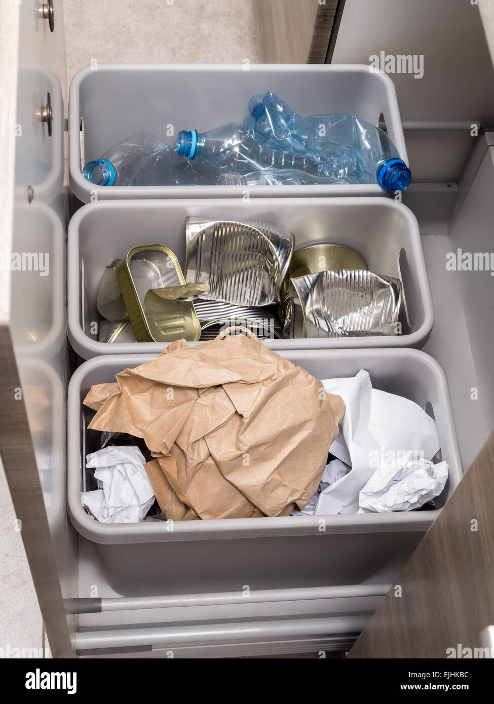Tres cubos de basura de plástico en la cocina armario con segregación de basura - botellas PET, papel y latas de metal Foto de stock