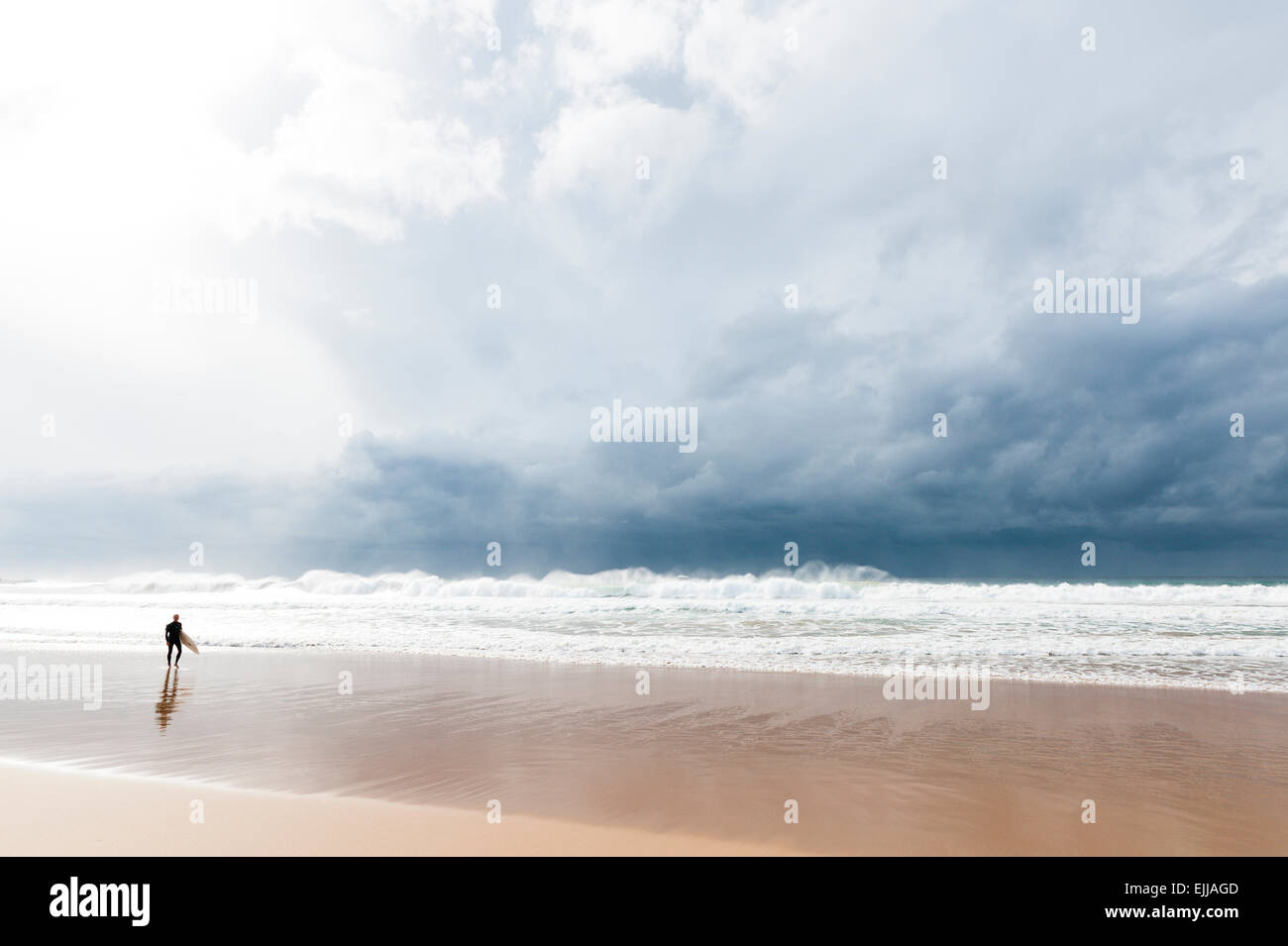 Sydney, Australia. Un surfista paseos a lo largo de la playa de Manly bajo el cielo negro grueso. Foto de stock