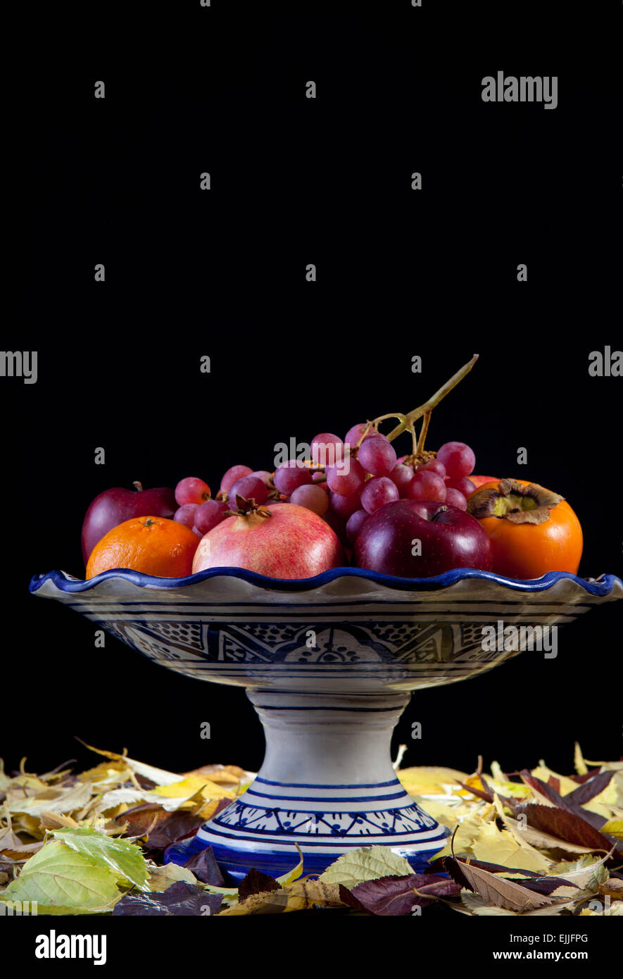 Frutero de cerámica con el otoño frutas aisladas sobre fondo negro.  Superficie lleno de hojas secas Fotografía de stock - Alamy