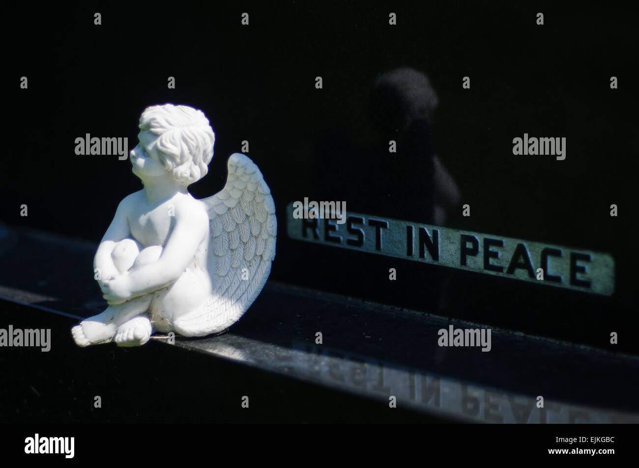 Ángel pequeño sentado sobre zócalo de granito negro lápida con la inscripción "st en paz" Foto de stock