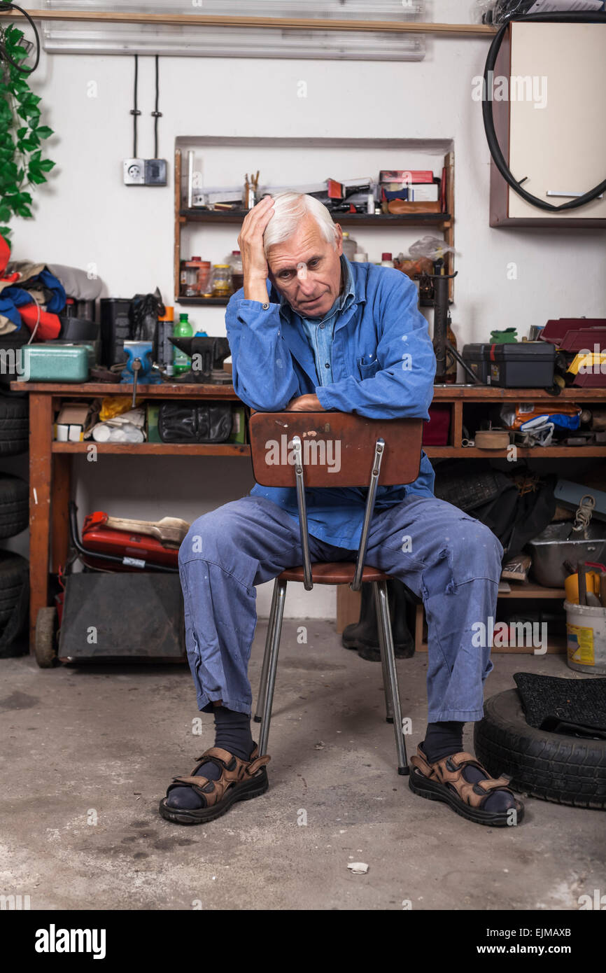 Retrato de frustrado trabajador senior sentado en la silla en su taller. Foto de stock