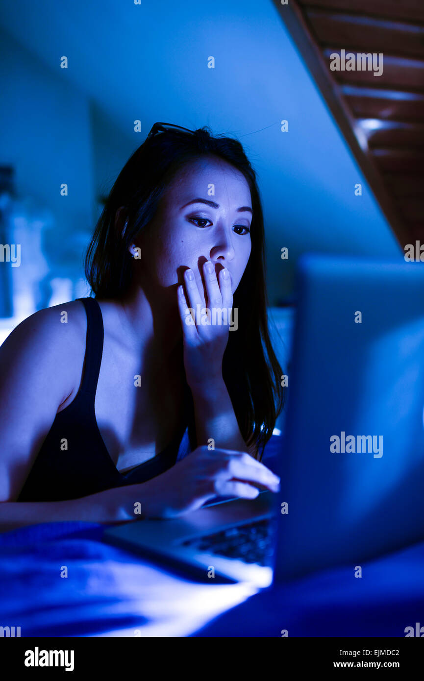 Víctima de acoso / acecho cibernético : Una guapa joven mujer china Asia chica utilizando una computadora portátil para ir en línea para leer sus correos electrónicos de control Facebook navegando por la web de la internet en su dormitorio en la noche UK Foto de stock