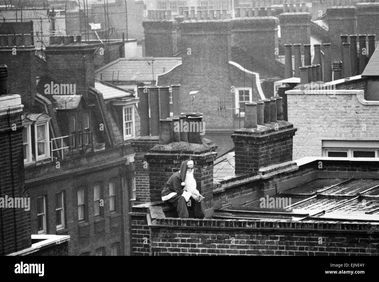 Papá Noel tiene tiempo de su apretada agenda para una rápida escapada de cigarrillos en el techo de una concurrida tienda de West End de Londres. El 23 de diciembre de 1970. Foto de stock