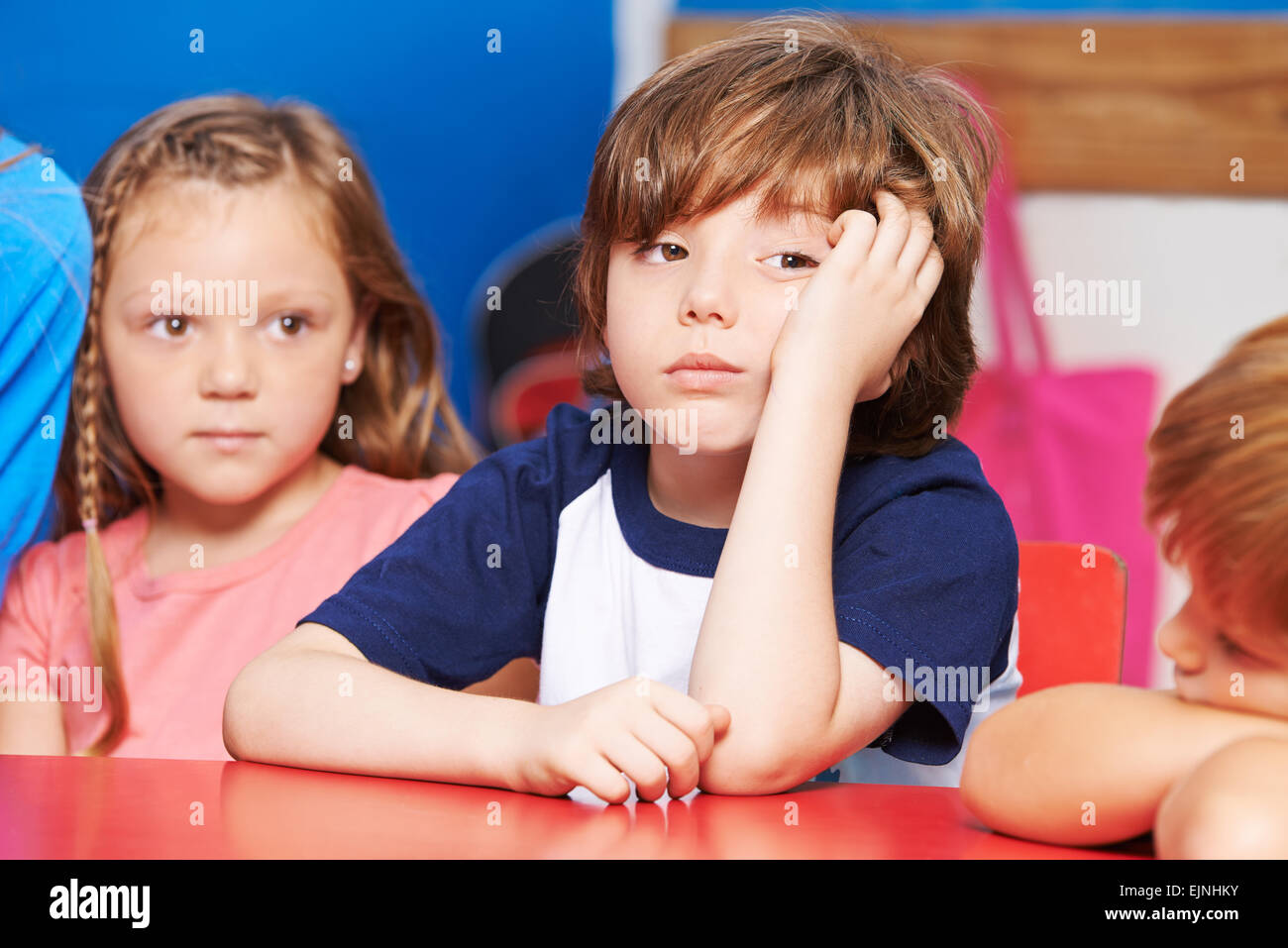 Niño es aburrido y sentado a la mesa en kindergarten. Foto de stock