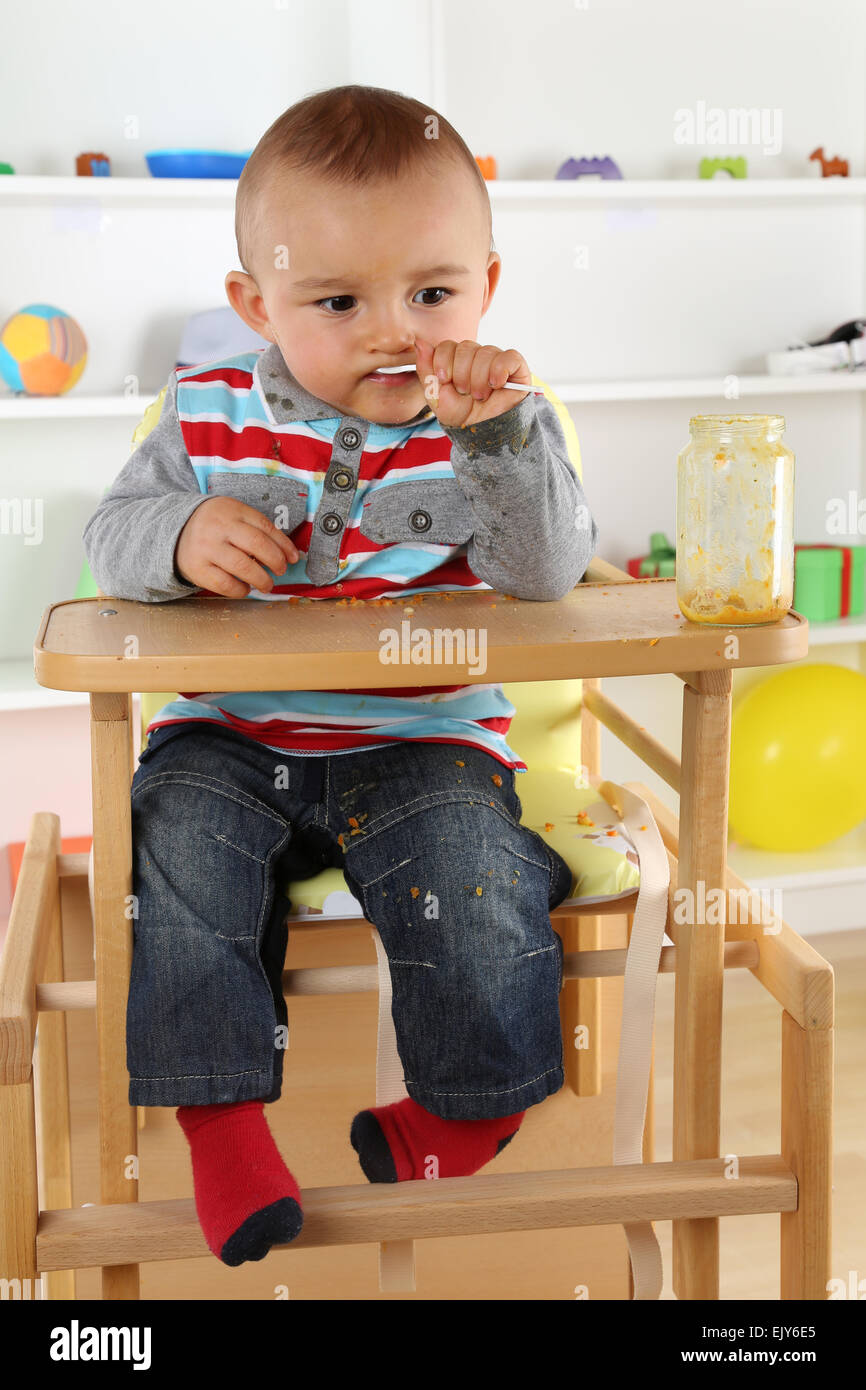 Niño pequeño comer la comida del bebé desde el cristal Foto de stock