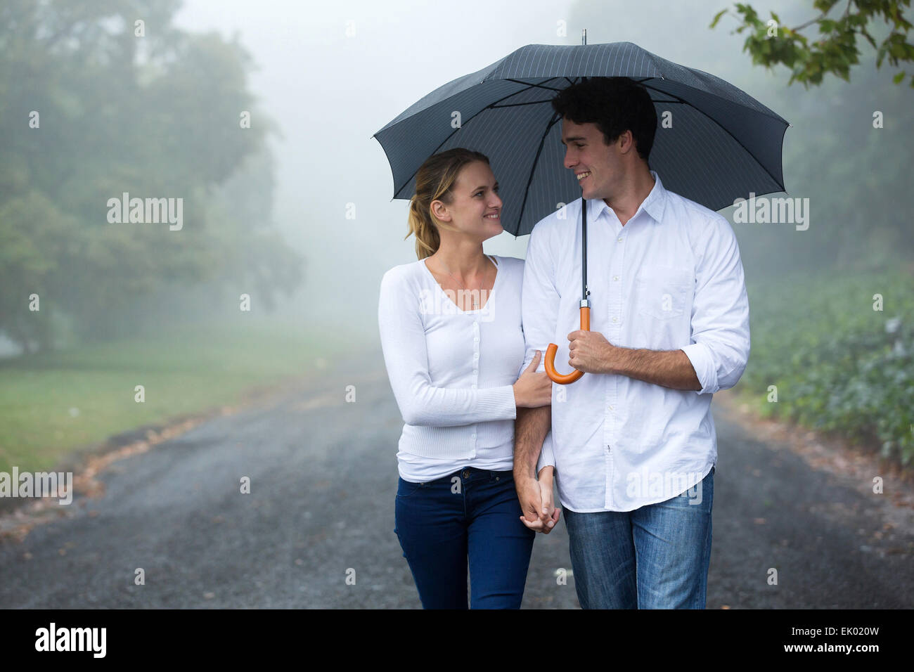 Hermosa pareja caminando bajo el paraguas en el bosque Foto de stock