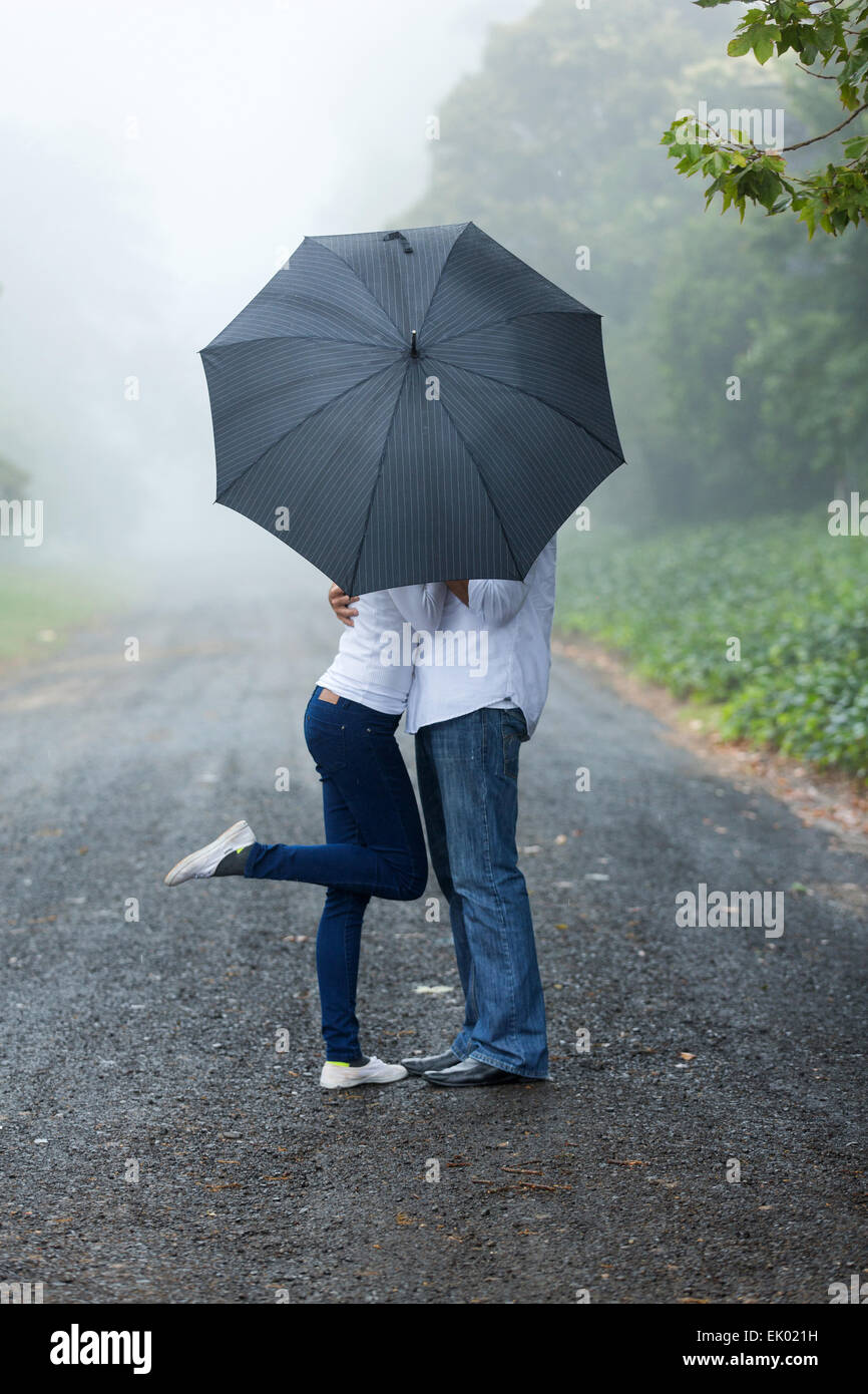 Romántica pareja joven escondiéndose detrás de los paraguas en la lluvia Foto de stock