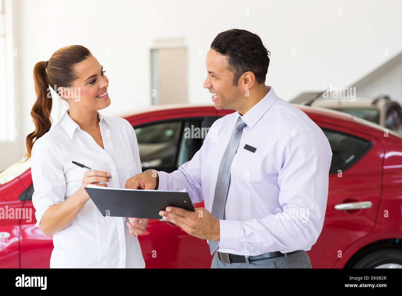Amable vendedor de coches de mediana edad que acaba de hacer una venta a clientes jóvenes Foto de stock