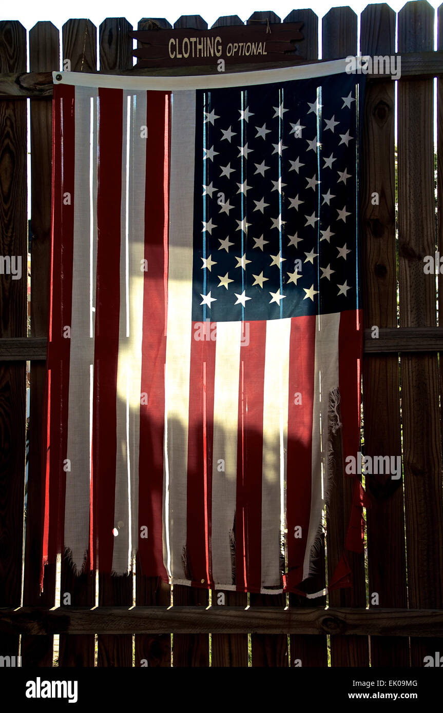 Un viejo y desgastado jirones de la bandera americana está colgando en una valla de stockade, retroiluminado por el sol de la mañana con un signo opcional de ropa encima. Foto de stock