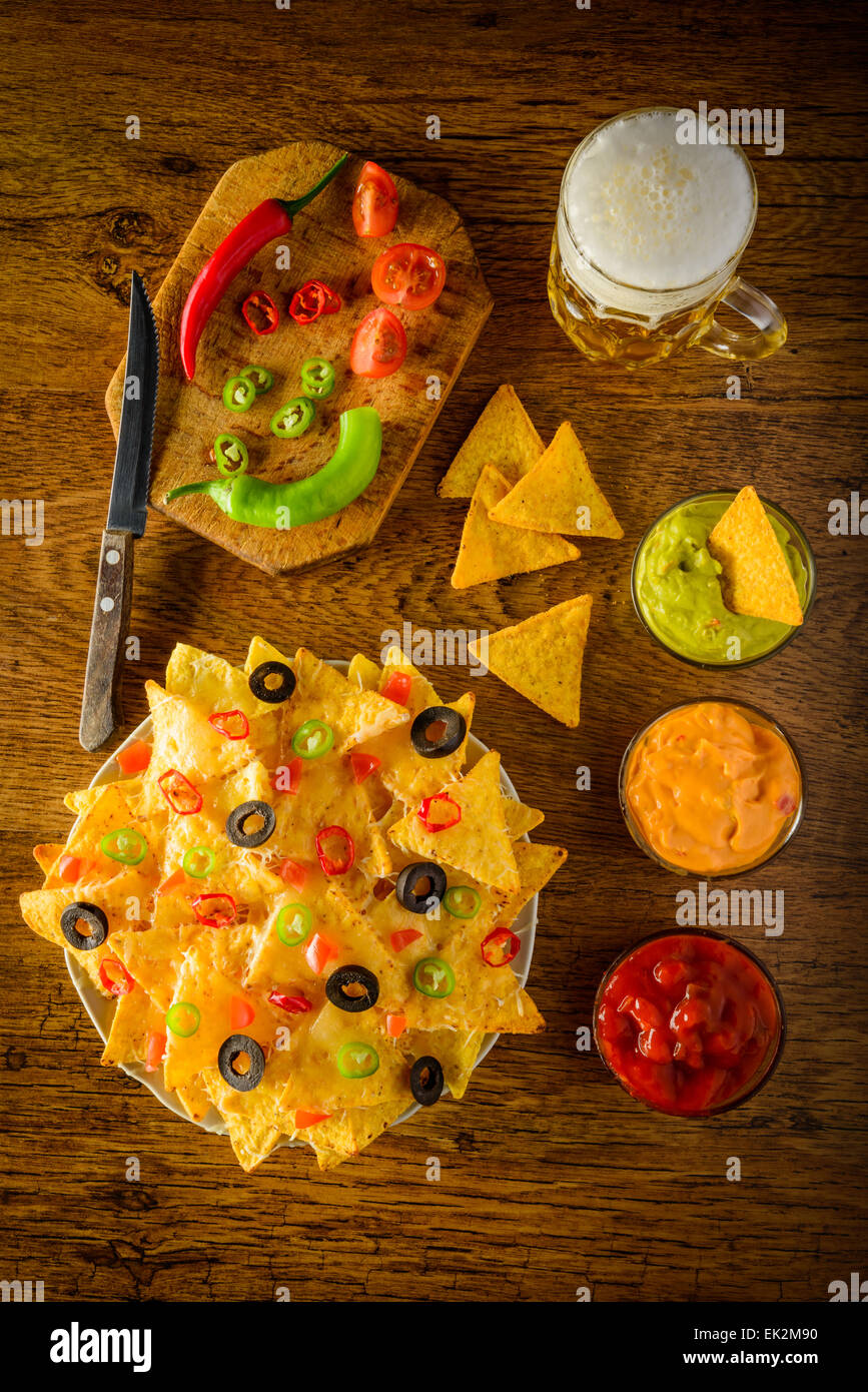 Nachos en un plato con salsa, queso y guacamole y jarra de cerveza Foto de stock
