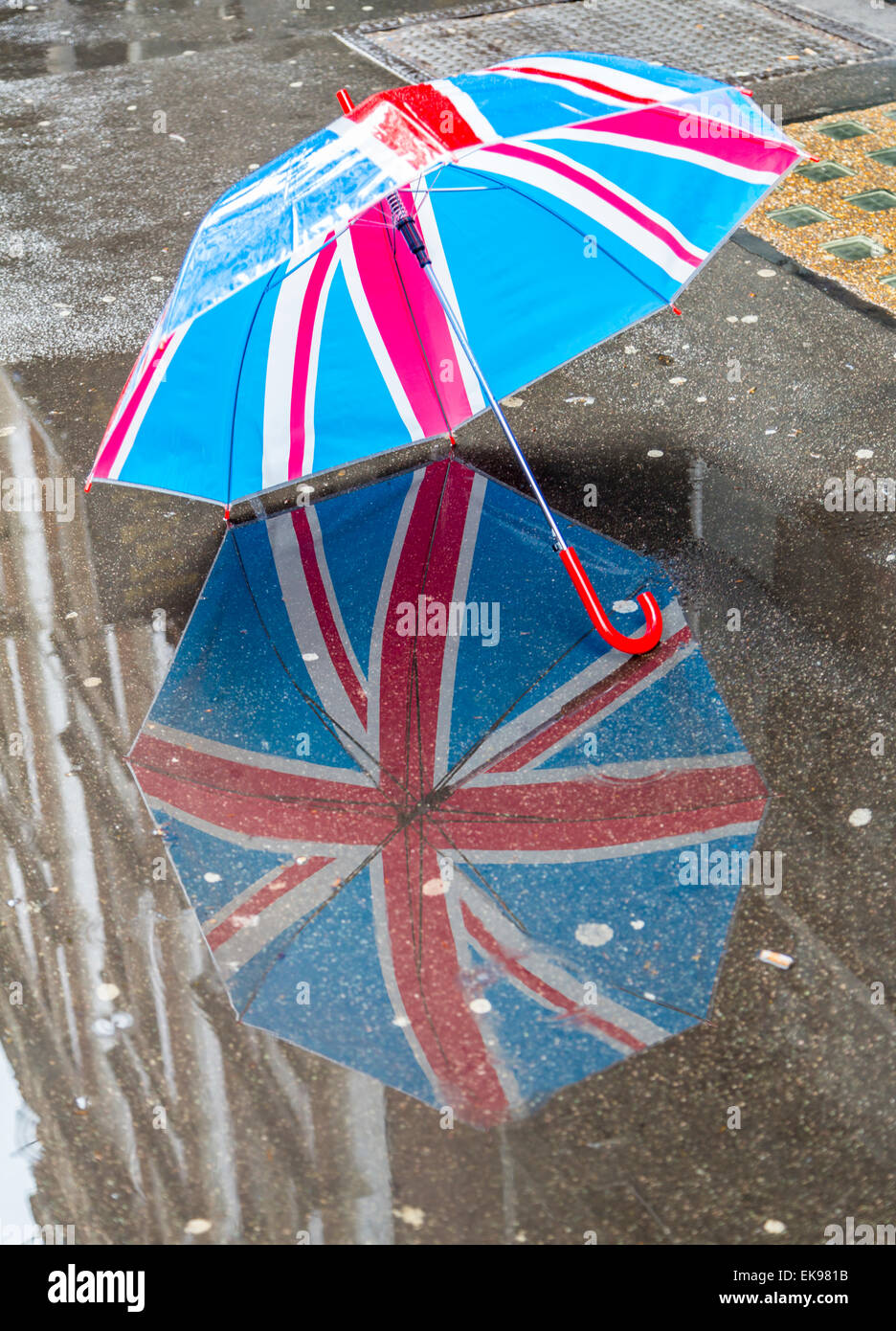 Una Union Jack paraguas reflejo en un charco en una lluvia de London Street, Londres, Inglaterra Foto de stock