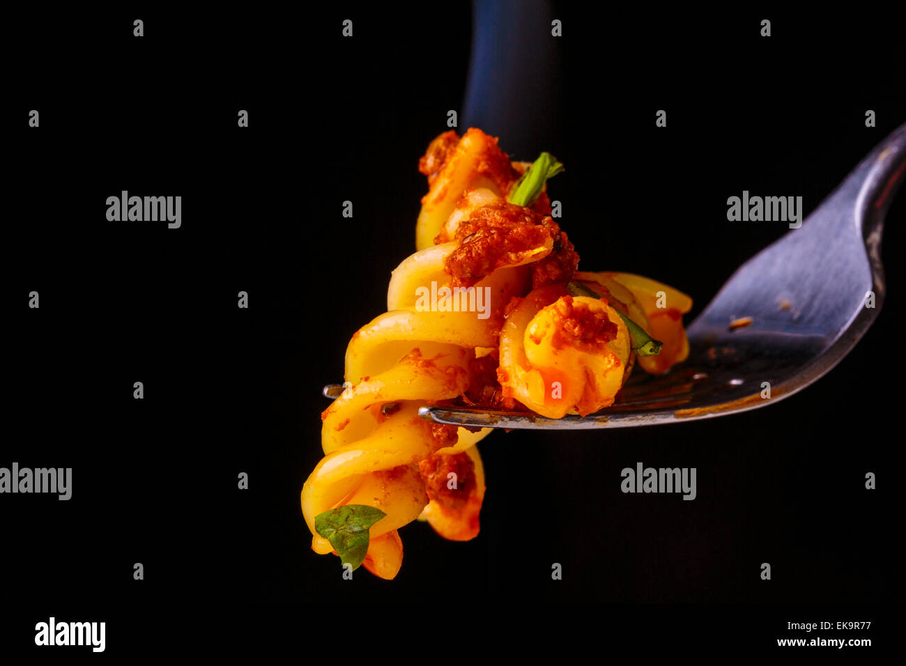 Una imagen de vapor caliente Fusilli pasta en una horquilla contra un fondo negro Foto de stock