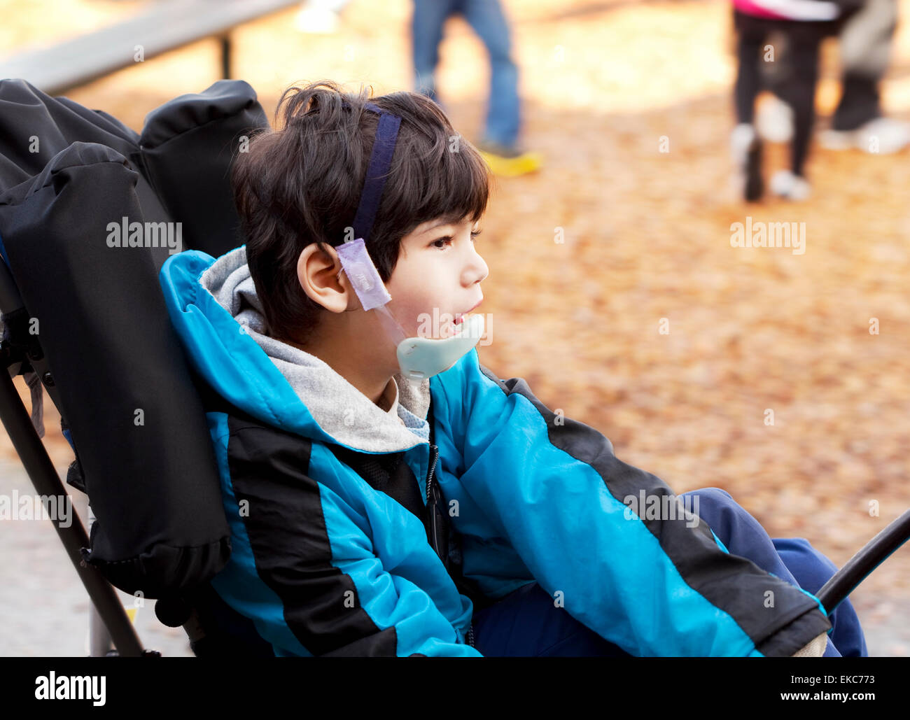 Minusválidos muchacho sentado en la silla de ruedas mientras juega en el campo de juegos Foto de stock