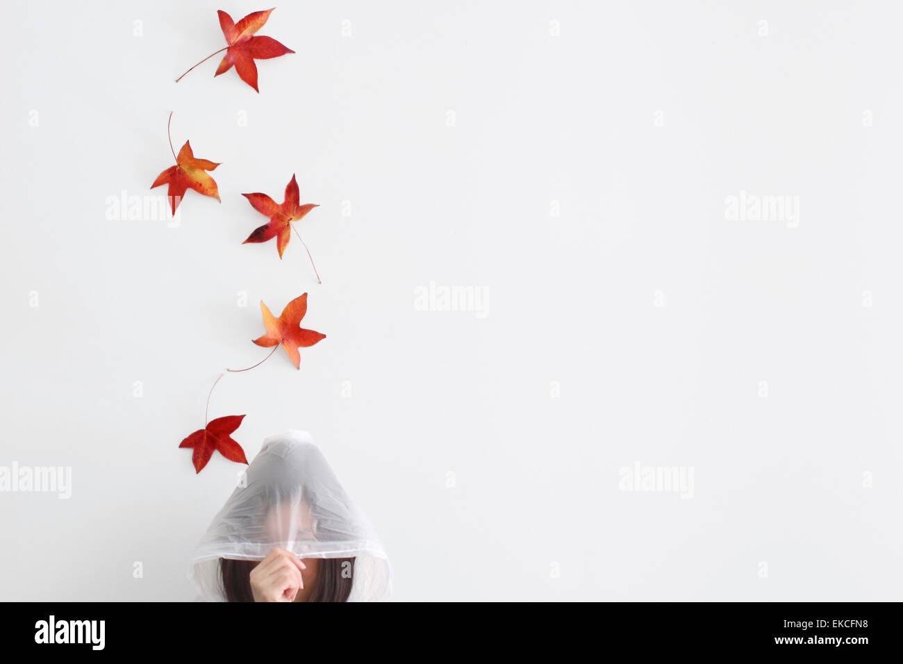 Hojas de otoño cayendo sobre una mujer en un impermeable Foto de stock