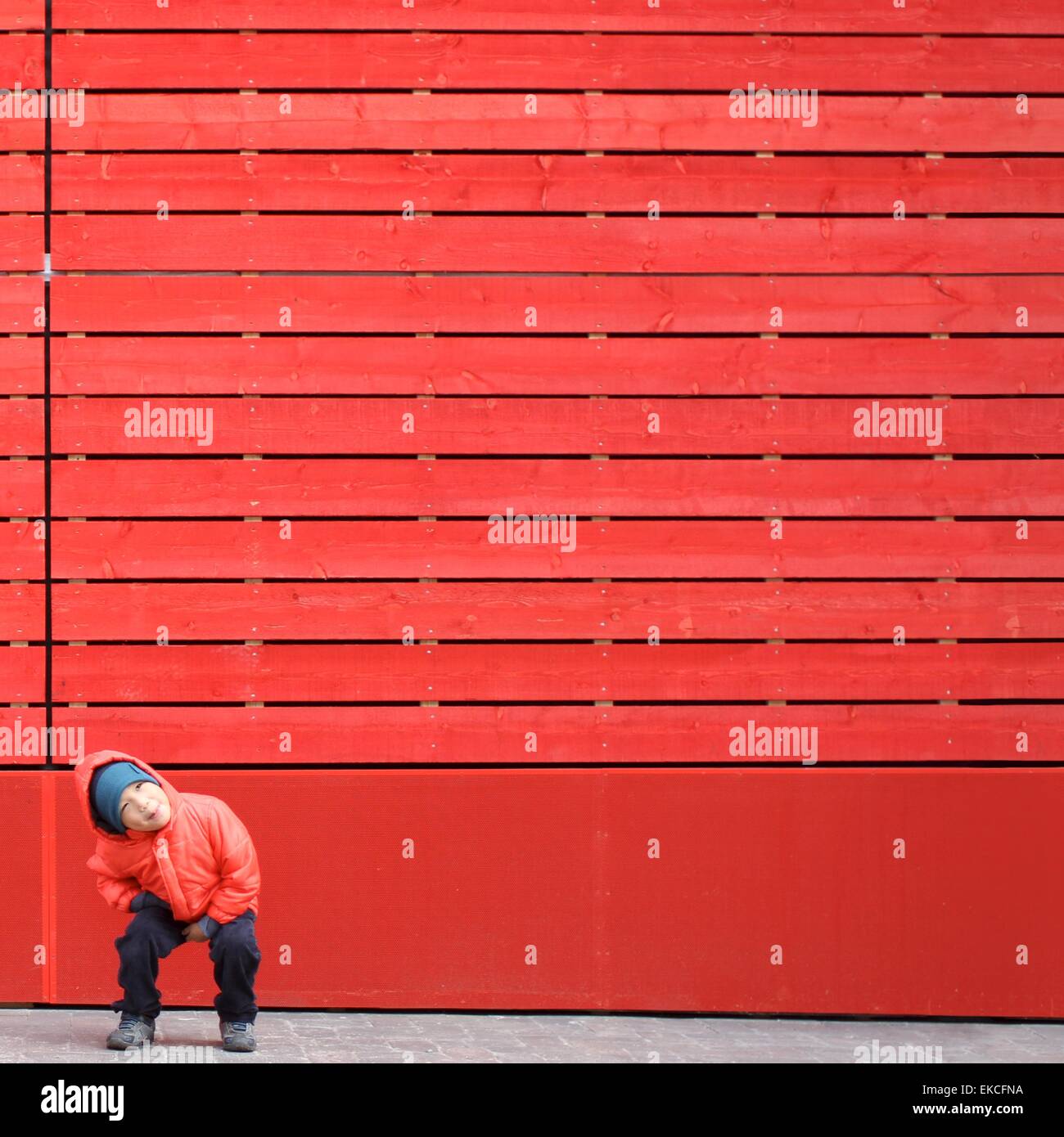 Chico en rojo ensuciando alrededor delante de una pared roja Foto de stock