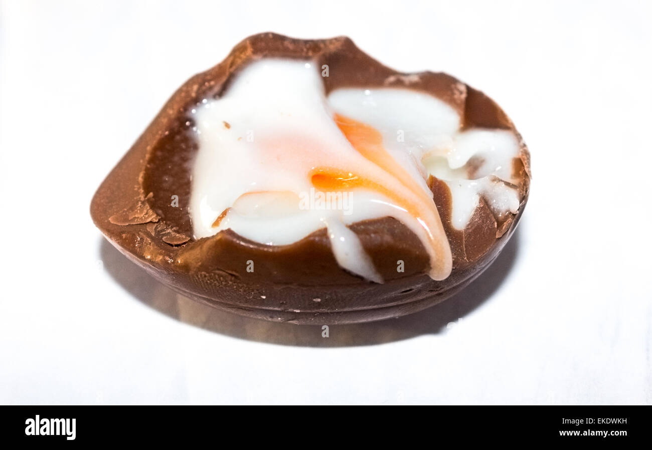 Una mitad comido chocolate rellenas de huevo con el azúcar y la yema de huevo de huevo relleno derramándose sobre el lado sobre un fondo blanco. Foto de stock